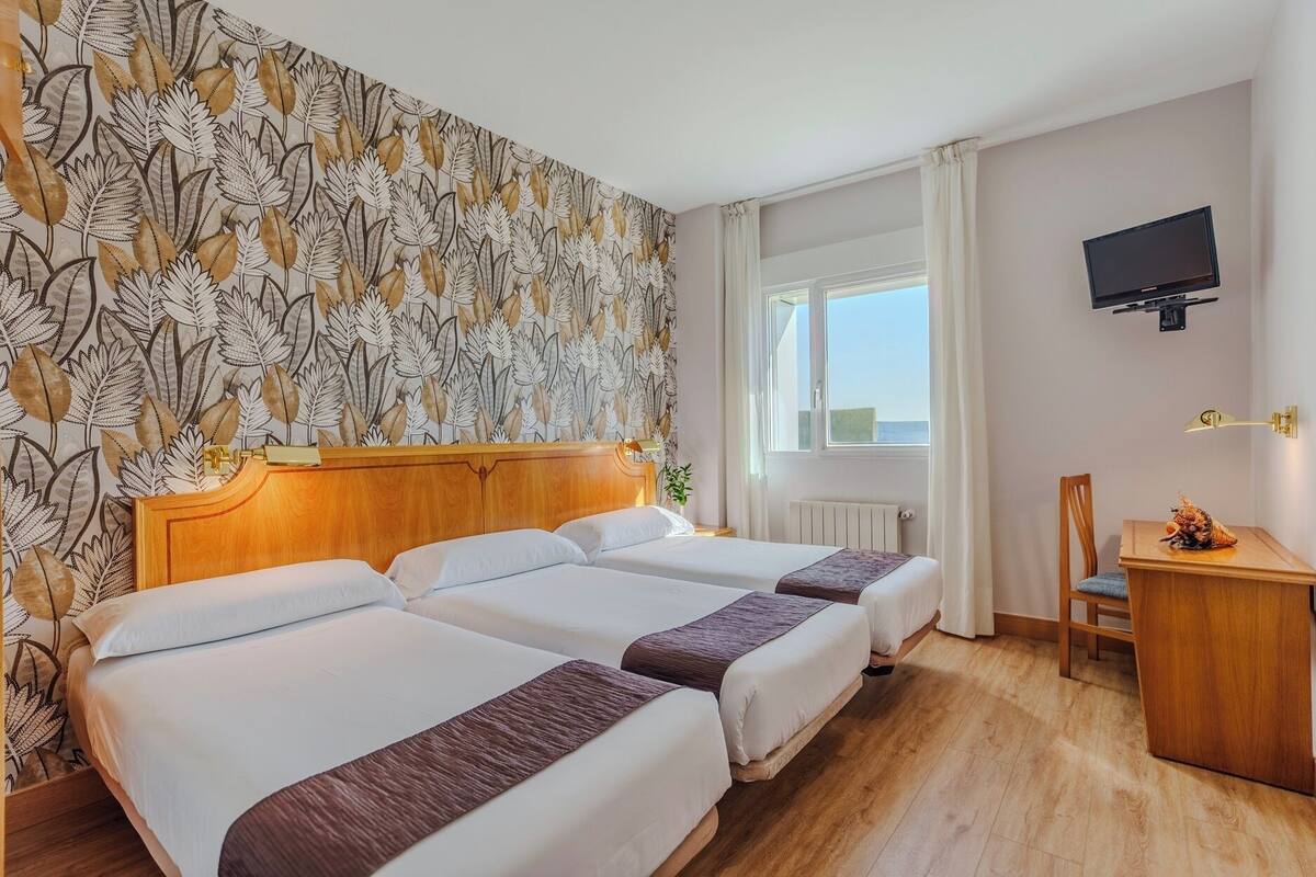 Une chambre d’hôtel avec deux lits, une tête de lit en bois, un bureau avec une chaise, une télévision et une fenêtre donnant sur un paysage agréable.
