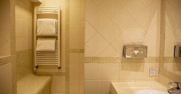 Uma casa de banho com parede revestida de azulejos, um porta-toalhas com toalhas, uma sanita, uma pia e um espelho.