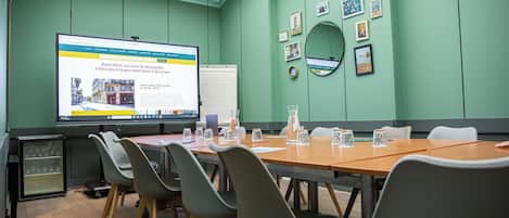 A conference room with a large screen displaying a hotel webpage, a whiteboard, and a table with chairs.