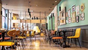 Um interior de restaurante moderno com teto de madeira, várias mesas e cadeiras, e obras de arte nas paredes.