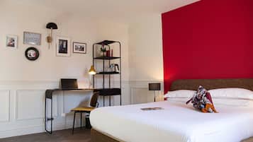 Hotelkamer met een bed, bureau met laptop, stoel, boekenkast en een rode accentmuur.