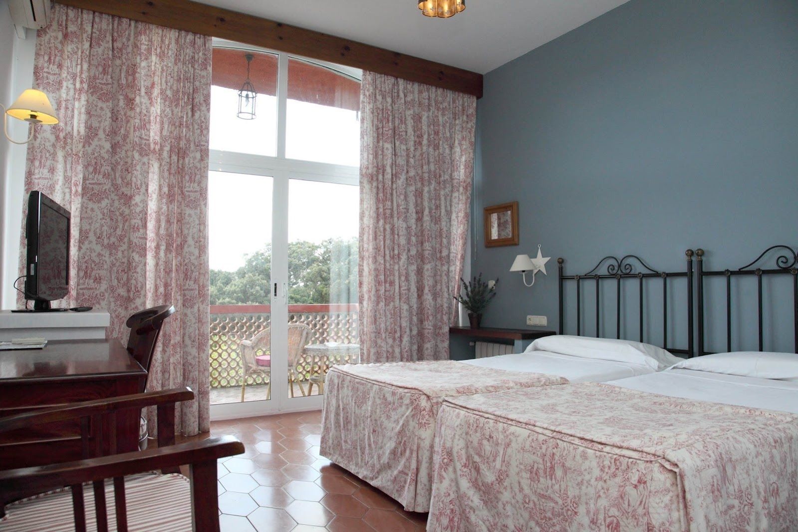 Un dormitorio con dos camas, un escritorio, una silla, un televisor y un balcón con vistas.