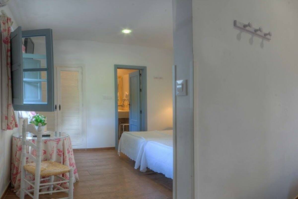 Habitación de hotel con dos camas, una mesita pequeña con una silla, un espejo y una lámpara en la pared.