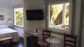 A cozy room with a bed, a television, a small table with chairs, and a window with a view of trees.