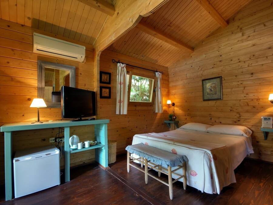 Acogedora habitación tipo cabaña con una cama, un escritorio con televisor, un refrigerador pequeño y una ventana con cortinas.