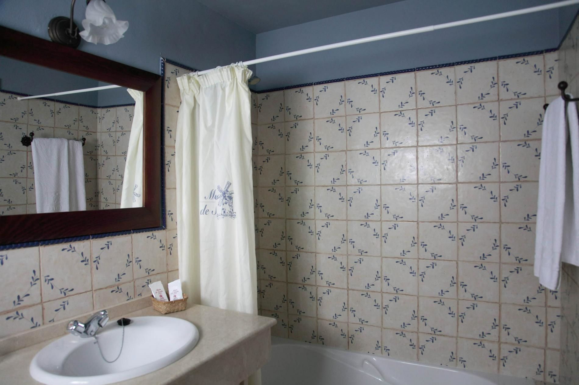 A bathroom with a white sink, a mirror, a shower curtain, and tiled walls.