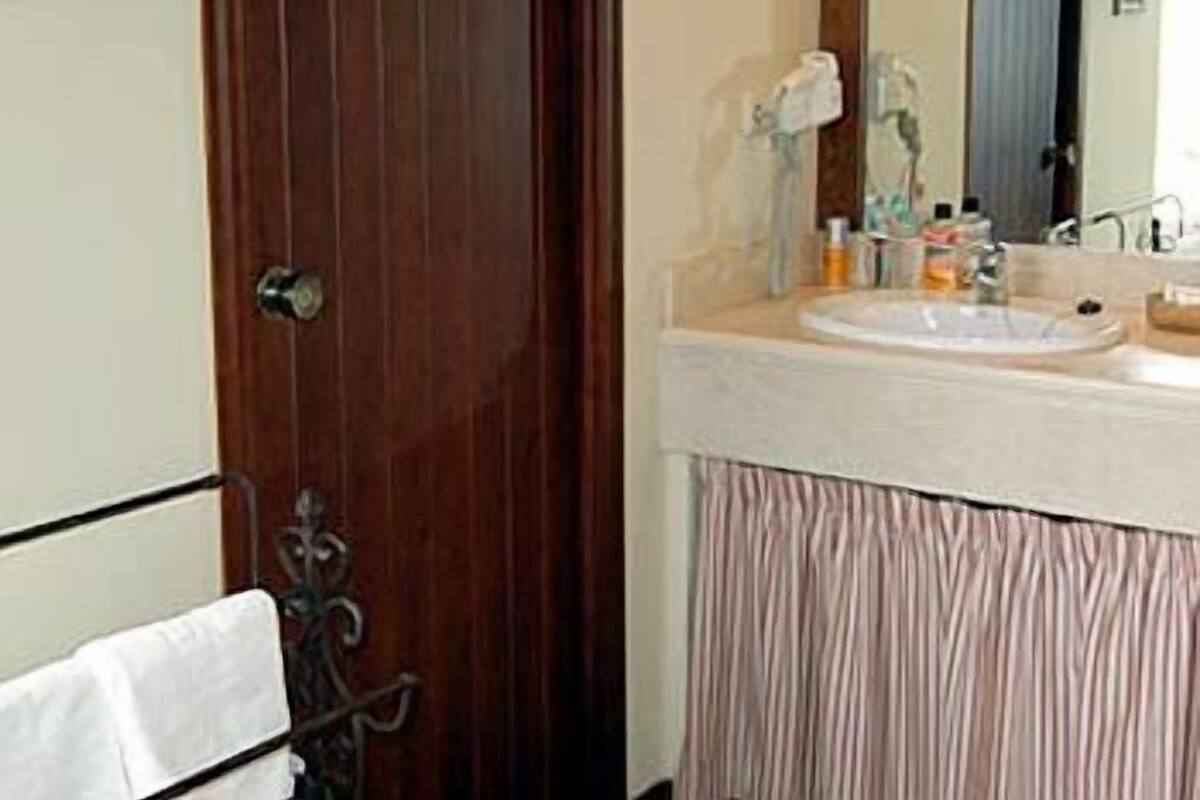 Un baño con puerta de madera, lavamanos con artículos de aseo y espejo.