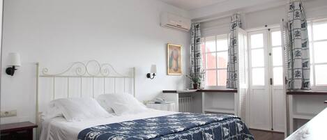 A bedroom with a bed, bedside tables, an air conditioning unit, a window with curtains, and a hanging light fixture.