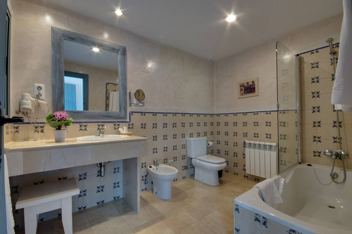 Un baño con bañera, dos inodoros, un bidé, un lavabo, un espejo y una planta en maceta.