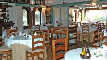 Un restaurante con varias mesas redondas y sillas de madera, en una sala con ventanales de arco y un techo alto.