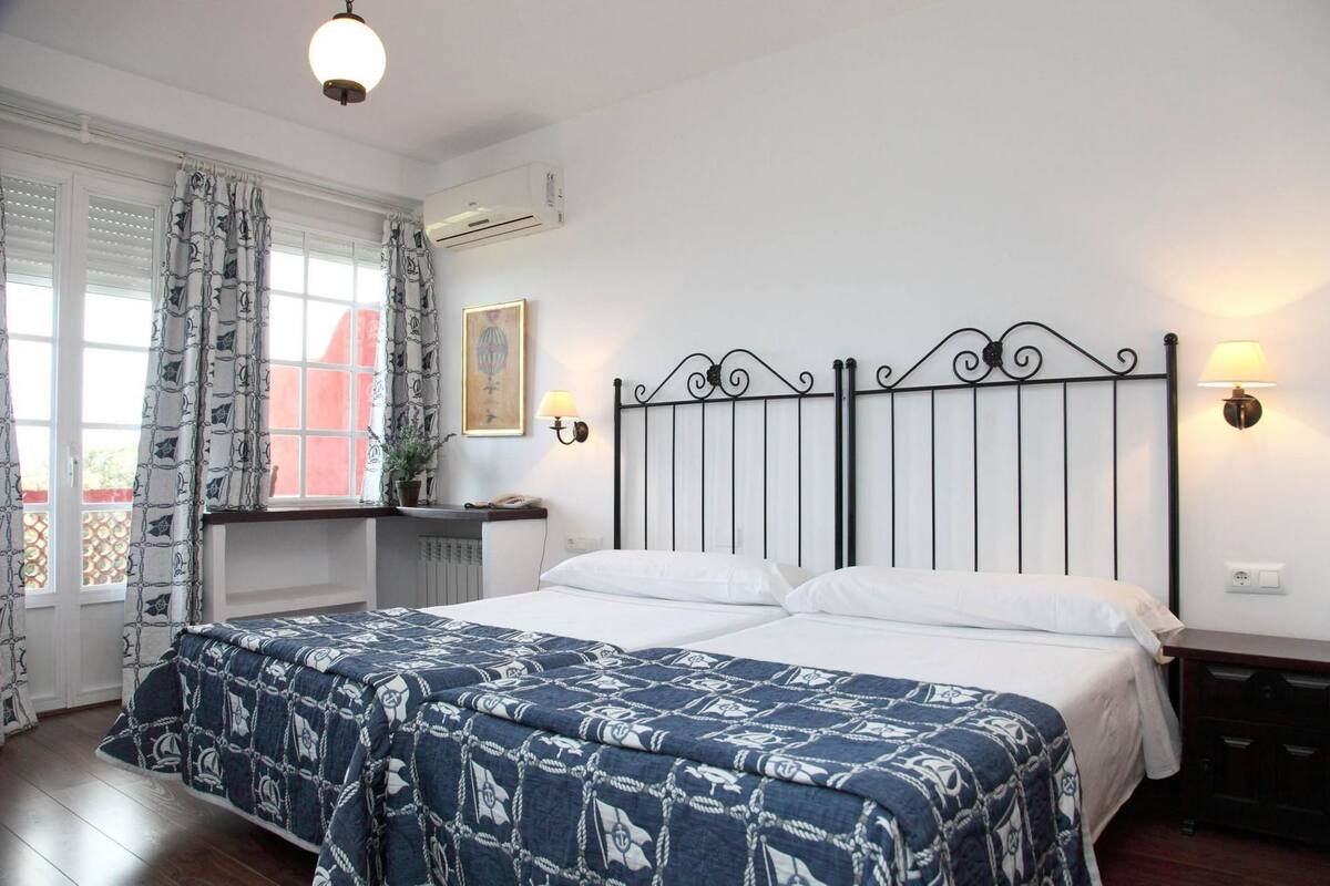 Un dormitorio con cama, cortinas, aire acondicionado, lámpara y radiador.