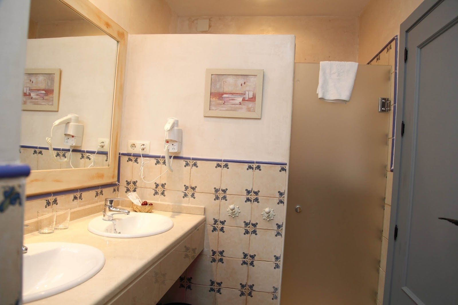 A bathroom with two sinks, a mirror, a towel hanging on the wall, and a shower area.