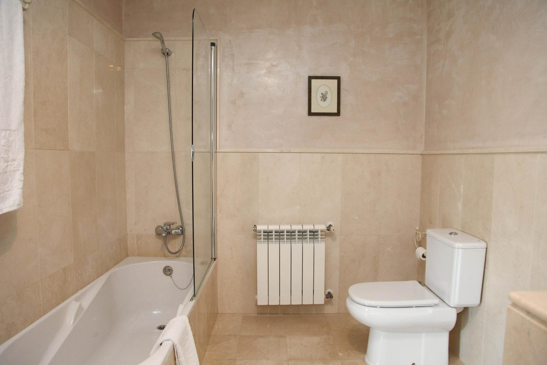 A bathroom with a bathtub, a toilet, a radiator, and a framed picture on the wall.