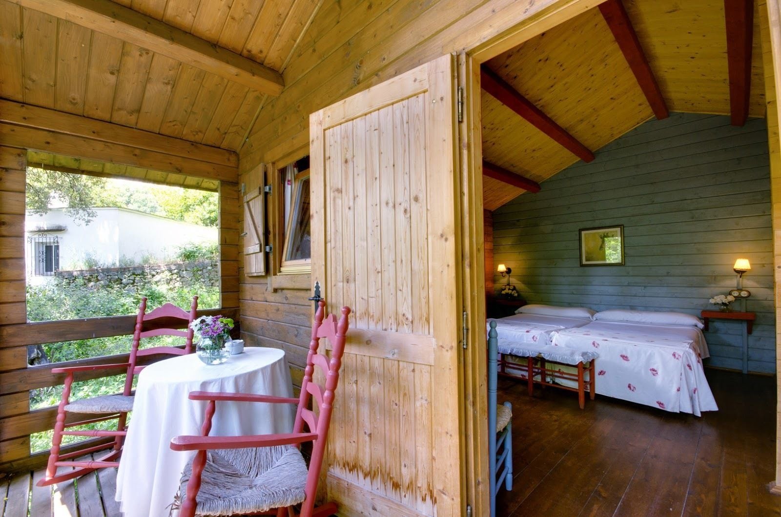 Una cabaña de madera con balcón, una mesa de comedor con sillas y un dormitorio con dos camas.