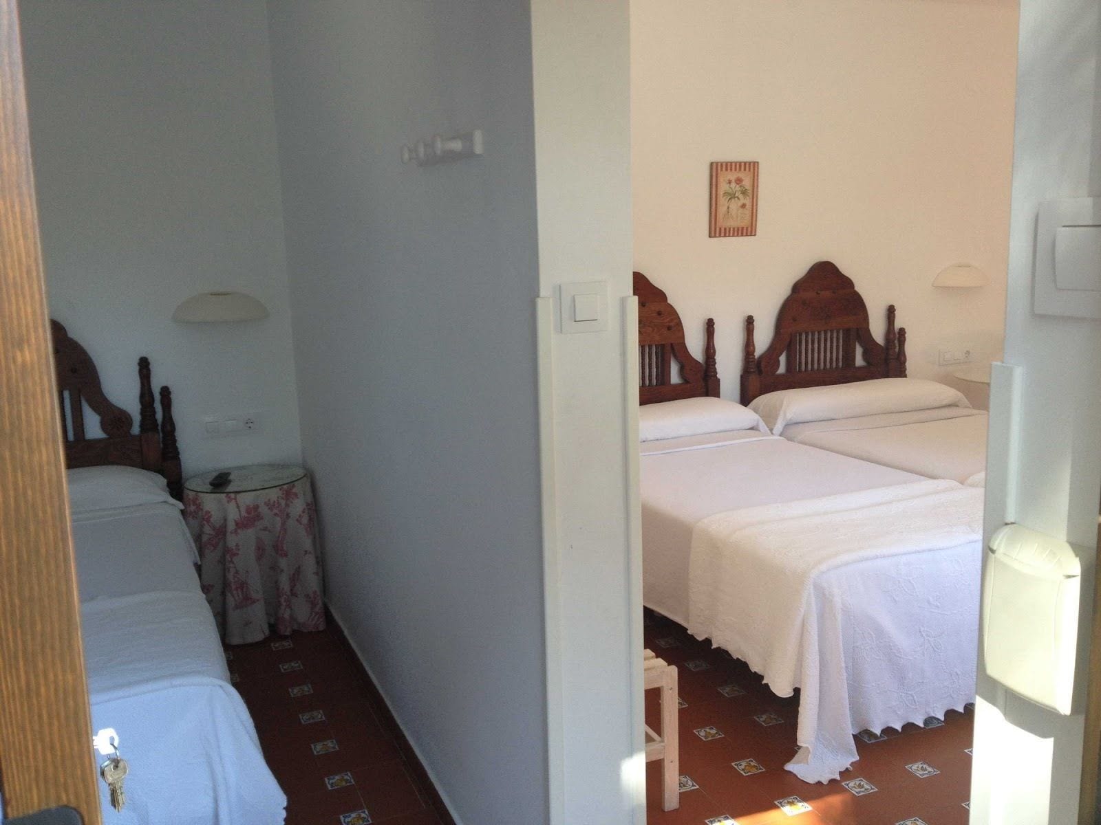 Un pasillo estrecho con una cama a la izquierda y dos camas con cabeceros de madera a la derecha.