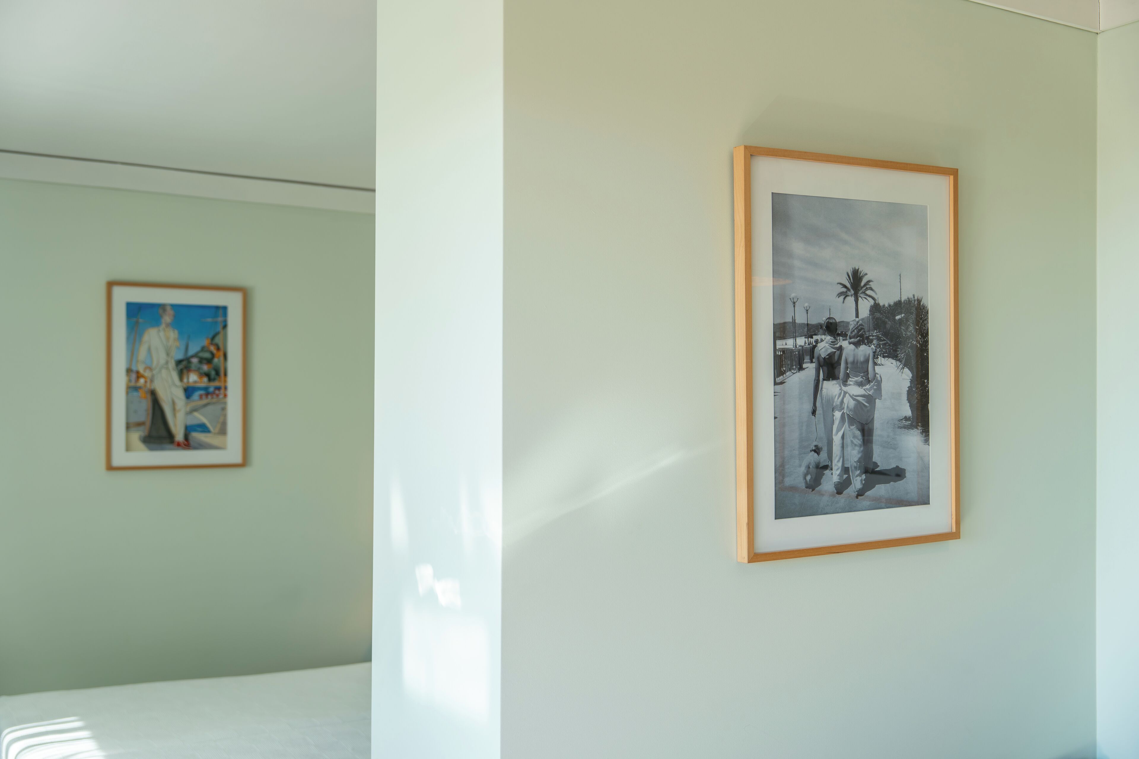 A room with two framed artworks on the wall, a bed, and a window allowing natural light.