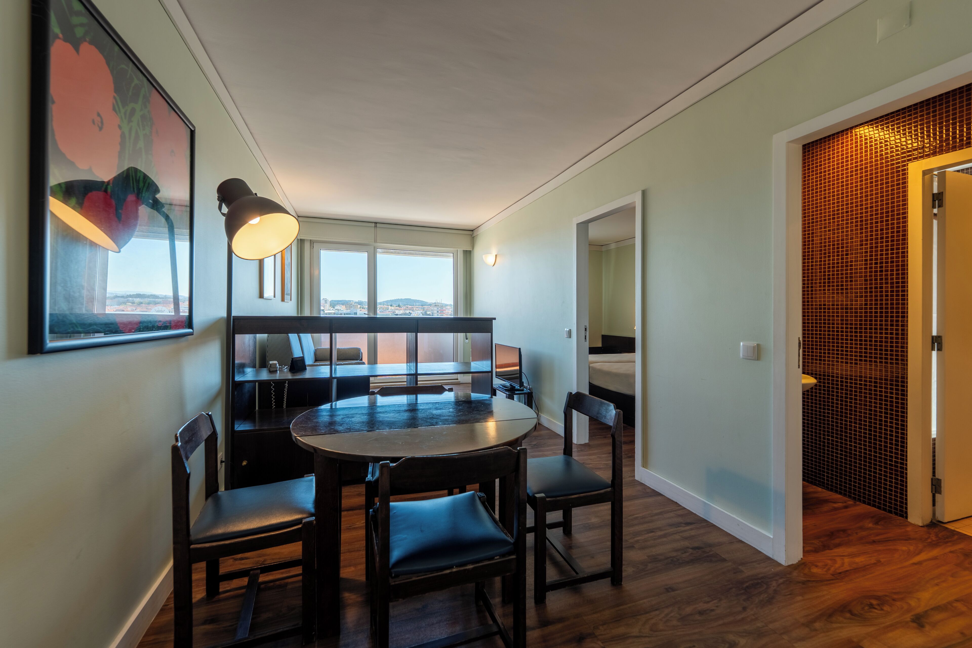 A dining area with a round table and four chairs, a large window with a view, and a door with a patterned wall.
