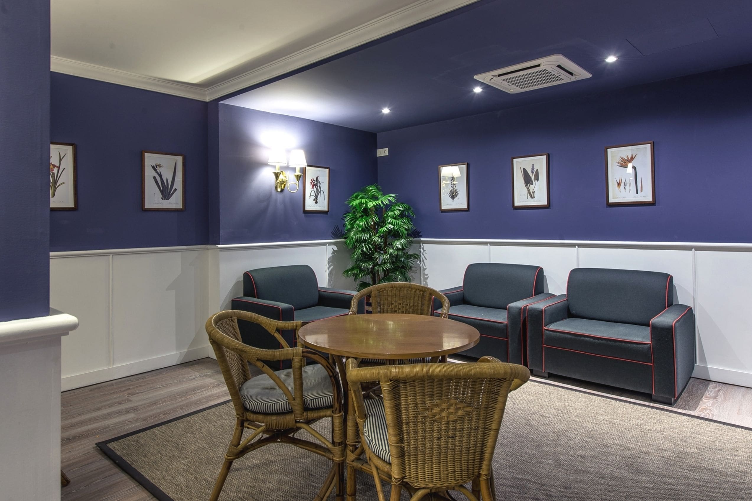 A conference room with a round table, two sofas, and wicker chairs.
