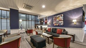 A modern lounge area with a sofa, chairs, and a coffee table. There is a wall with a colorful artwork and a small table with a lamp.