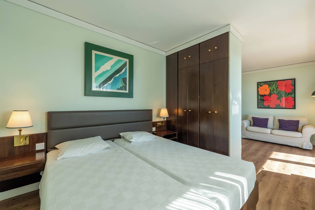 A hotel room with a large bed, two bedside tables with lamps, a wardrobe, and a sofa in the corner.