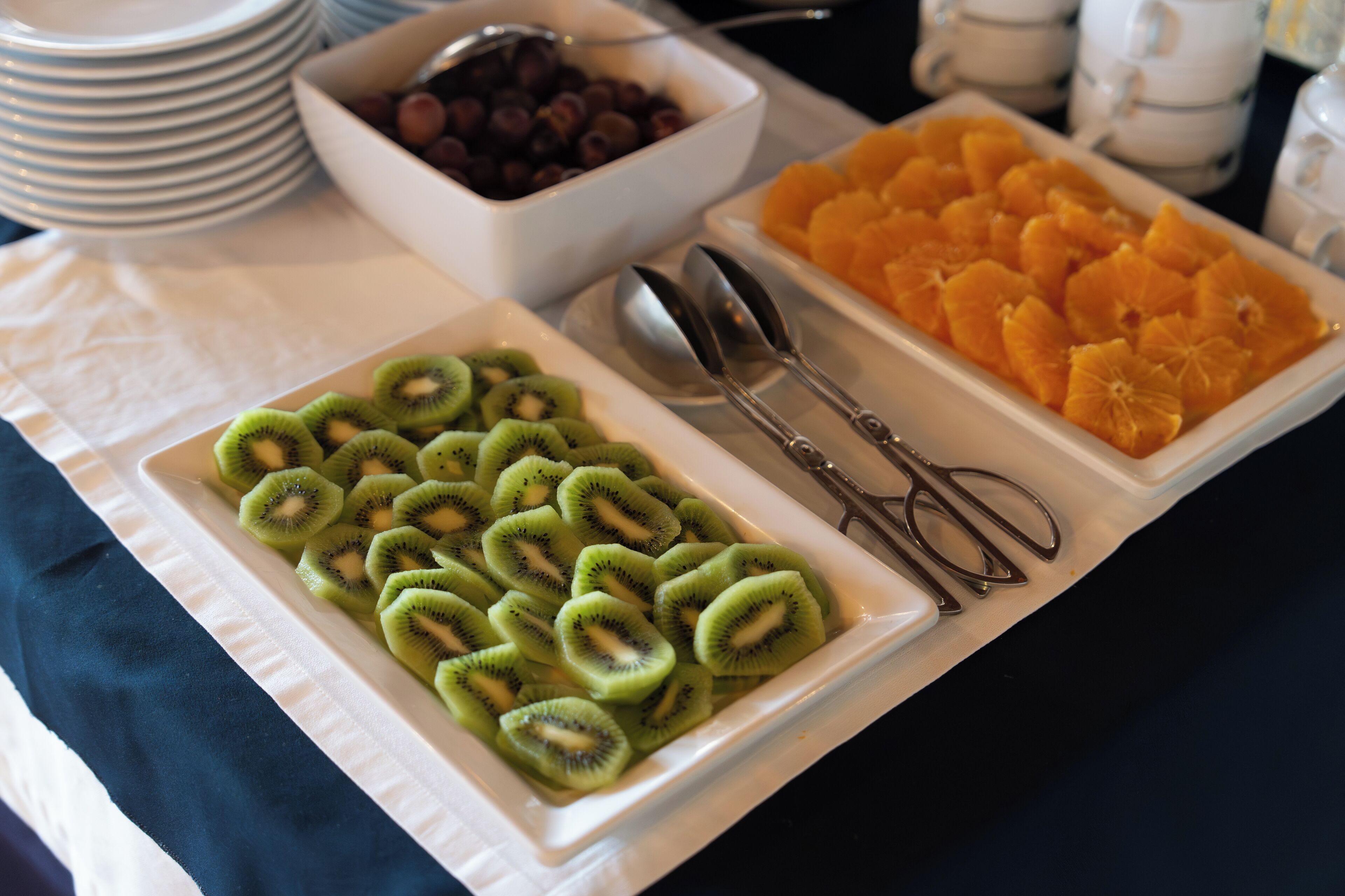 Une table de buffet avec des assiettes de tranches de kiwi et de quartiers d’orange.