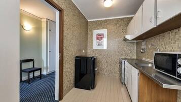 A compact kitchen with a refrigerator, microwave, sink, and tiled backsplash.
