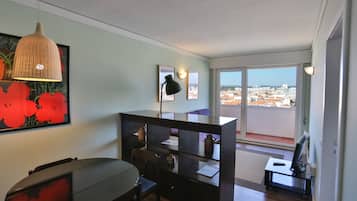 A modern room with a dining table, chairs, a black desk, and a large window offering a city view.