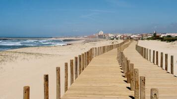 Une promenade en bois qui mène à une plage, d’où l’on a une vue dégagée sur l’océan et les bâtiments situés au loin.