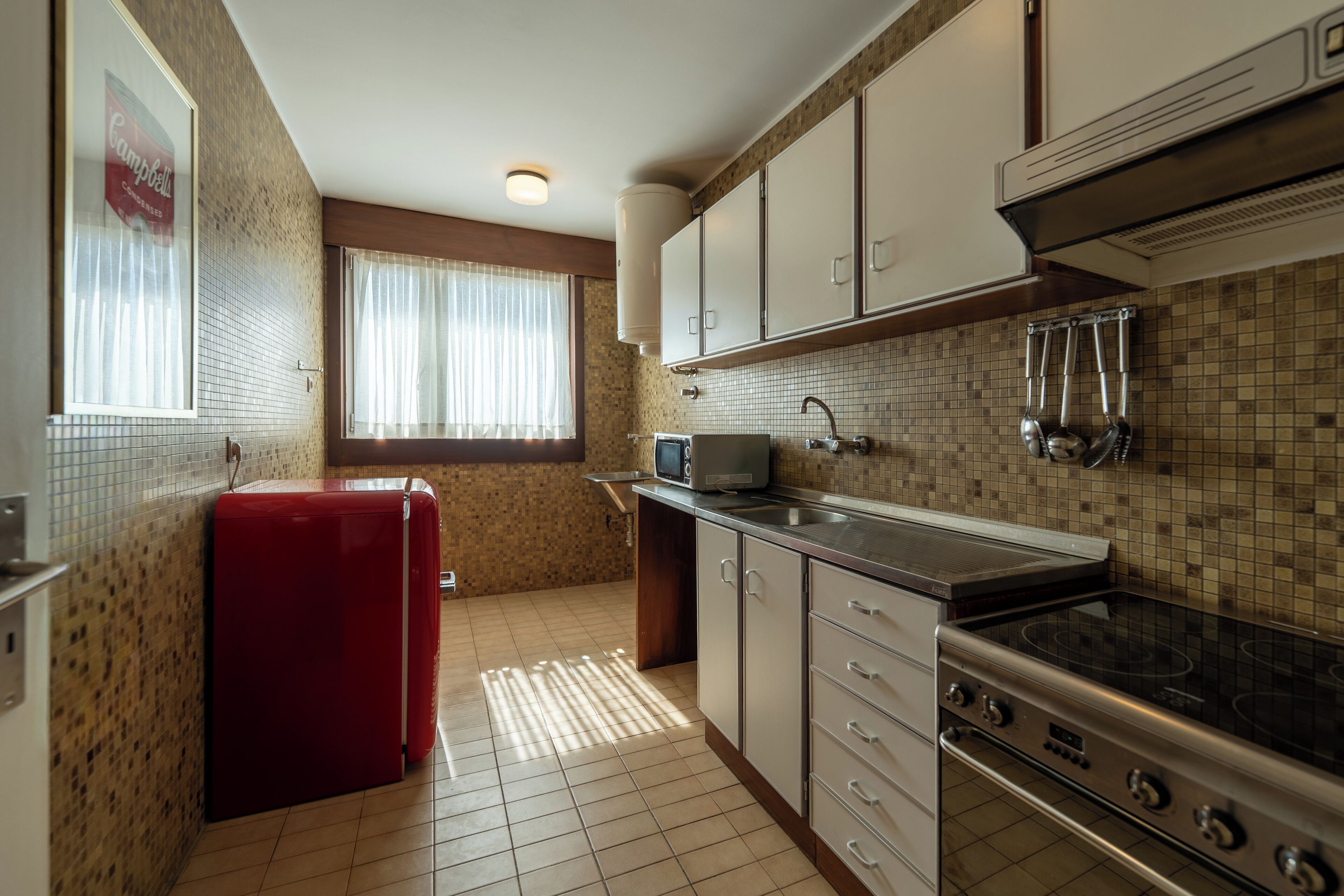 A compact kitchen with a refrigerator, stove, microwave, and tiled backsplash.