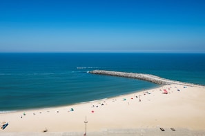 A beach with a rocky breakwater, sandy shore, and umbrellas.