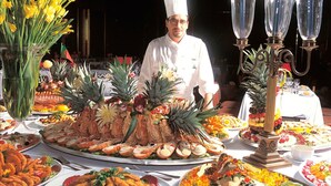 A chef standing behind a large, elaborate buffet spread with various dishes and decorations.