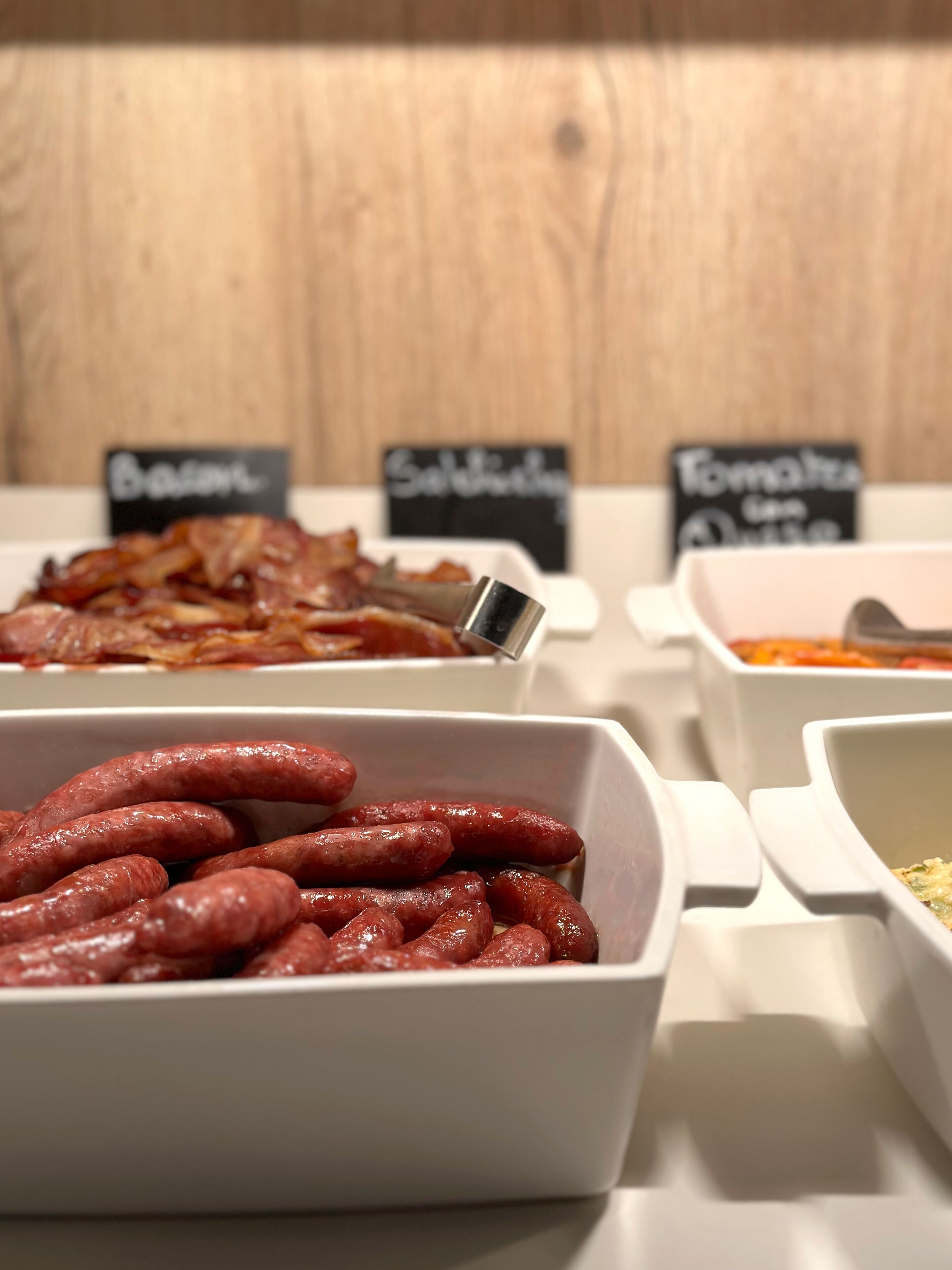 Buffet-pöydässä on tarjolla monipuolinen valikoima ruokia, kuten makkaroita, pekonia ja muita herkkuja.