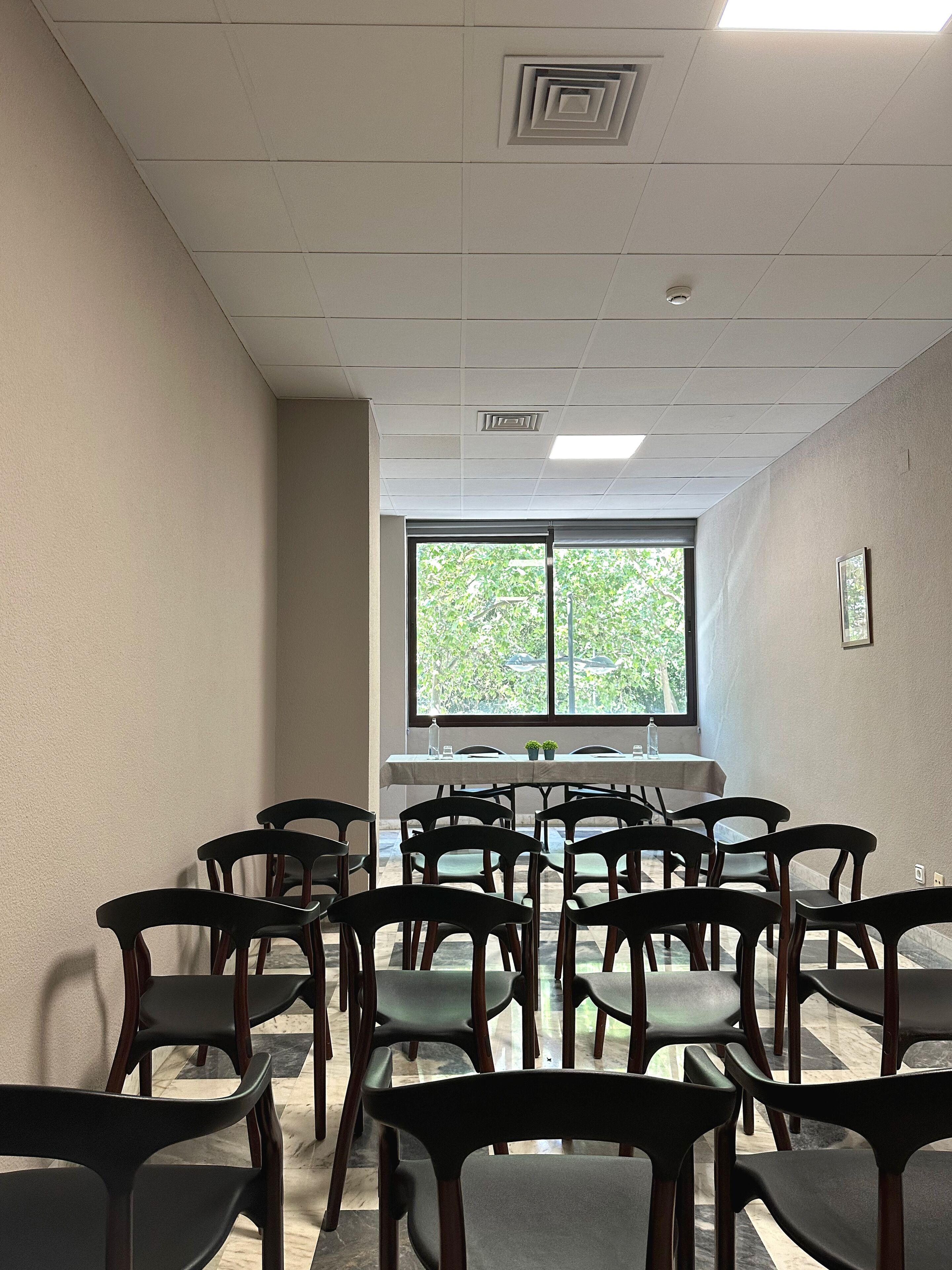 Sala de conferências com uma grande janela, várias cadeiras e uma mesa com garrafas de água e copos.
