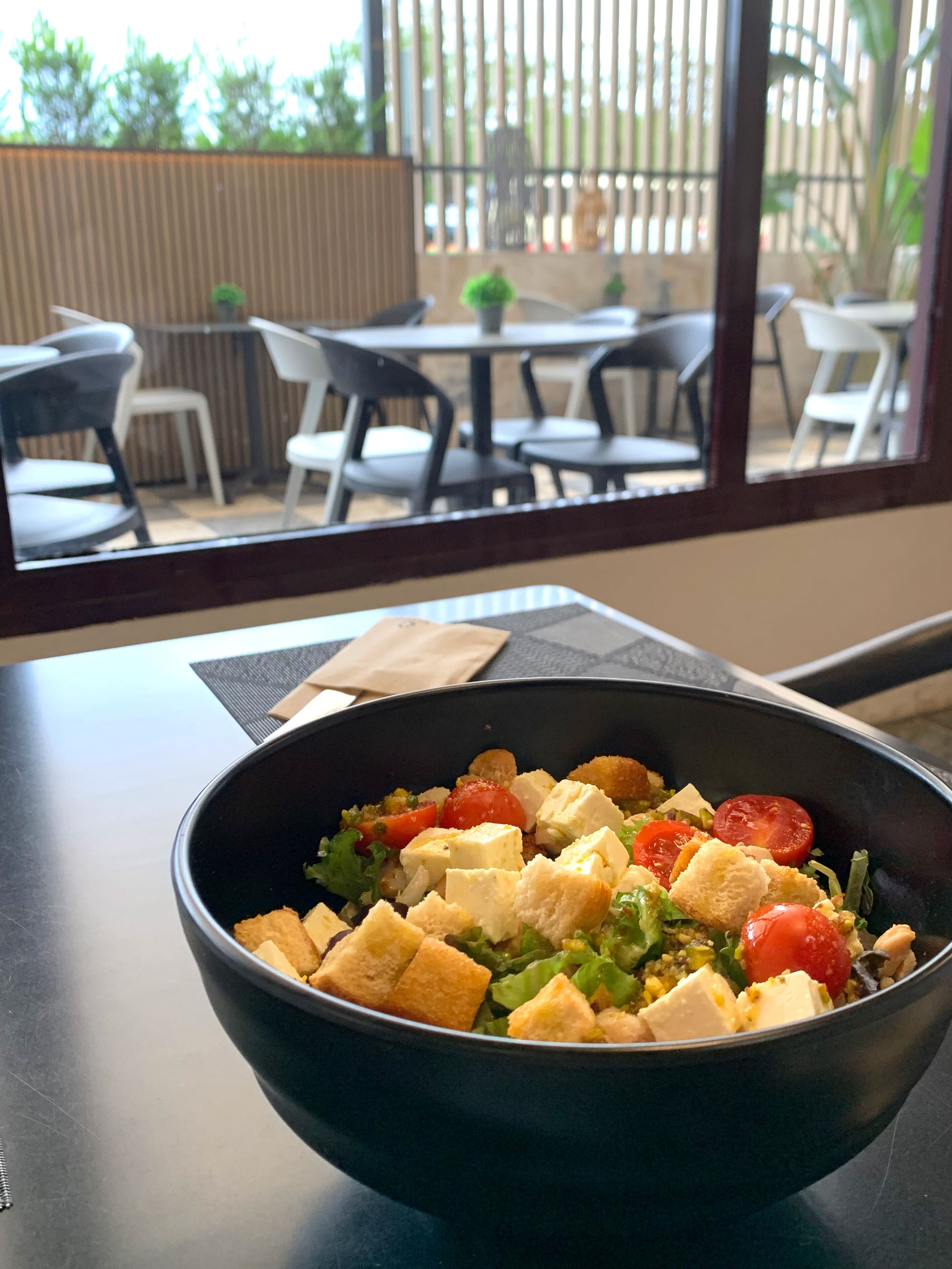 Un tazón de ensalada sobre una mesa con vista a un área de asientos al aire libre.