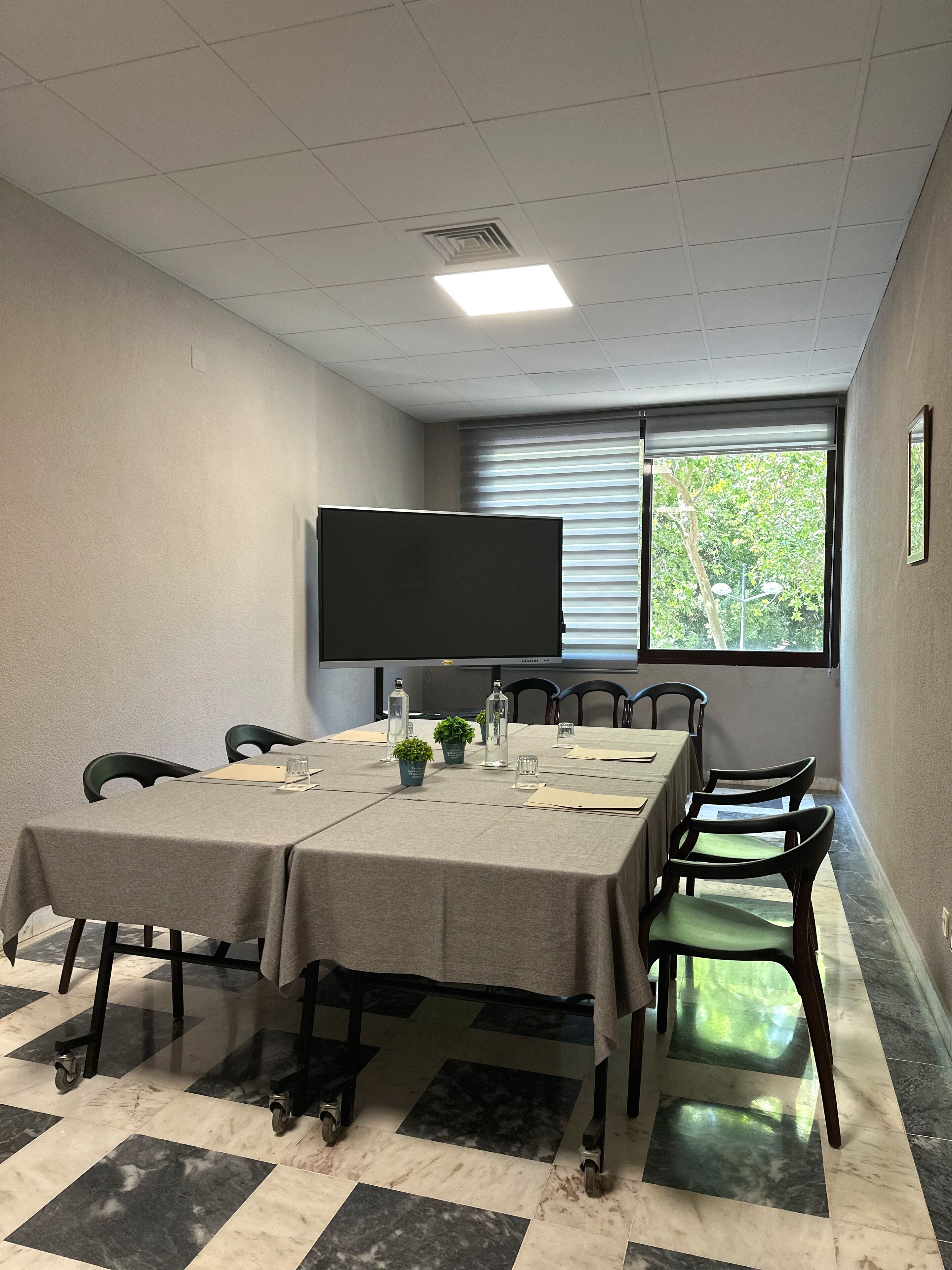 Une salle de conférence équipée d’une grande table, de chaises, d’un écran de projection et d’une fenêtre avec des stores.
