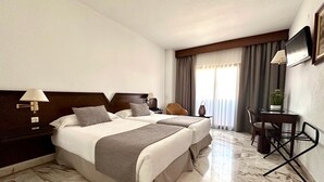 A hotel room with two beds, a desk, a chair, a TV, and a window with curtains. - Hotel Turia Valencia (Valencia)