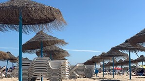A beach with thatched umbrellas and stacked plastic chairs. - Hotel Turia Valencia (Valencia)