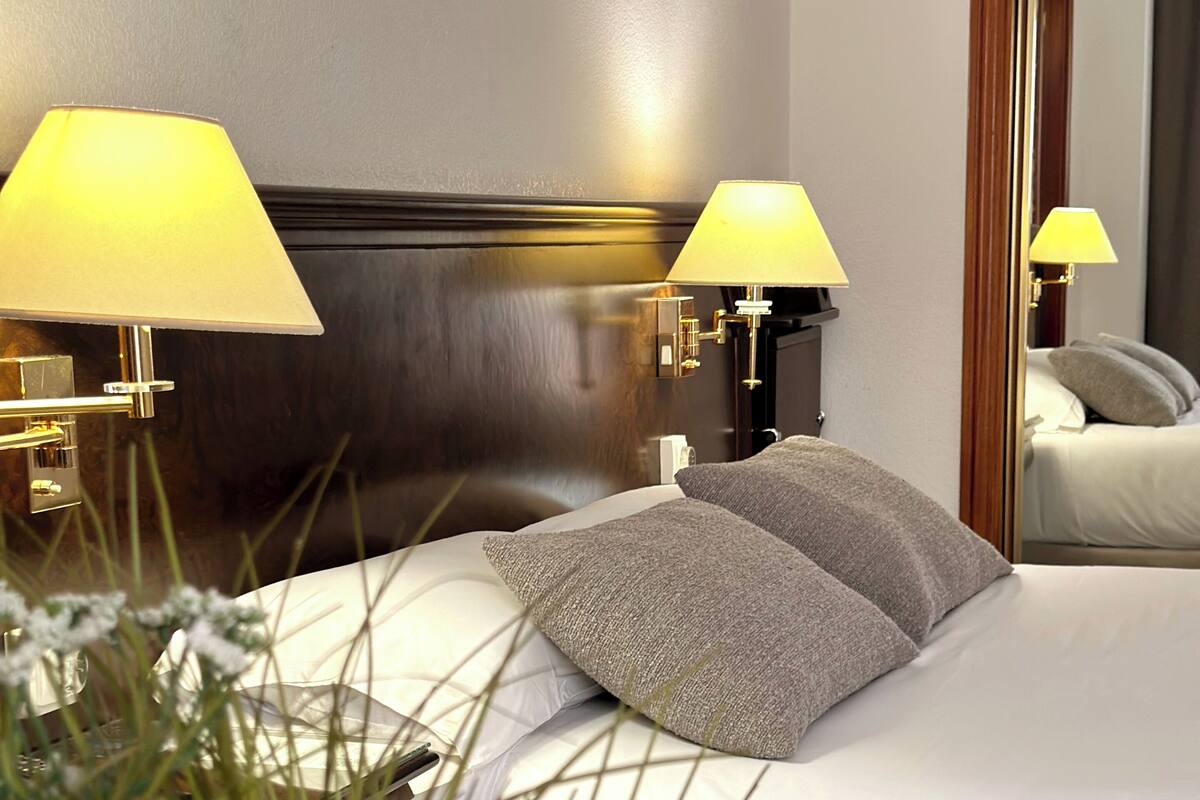 A hotel room with a large bed, two bedside lamps, a wooden headboard, and a mirror on the wall.