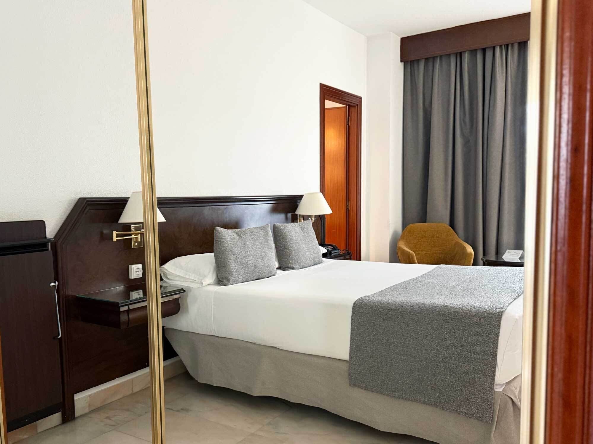 A hotel room with a large bed, a nightstand, a desk, a chair, and a wooden door.