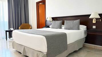 Habitación de hotel con una cama grande, dos lámparas de noche, cabecera de madera, un escritorio con silla y una ventana con cortinas.