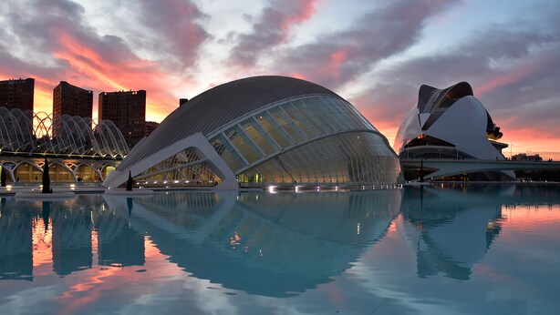 A modern architectural building with a unique curved design, reflecting in a calm body of water. - Hotel Turia Valencia (Valencia)