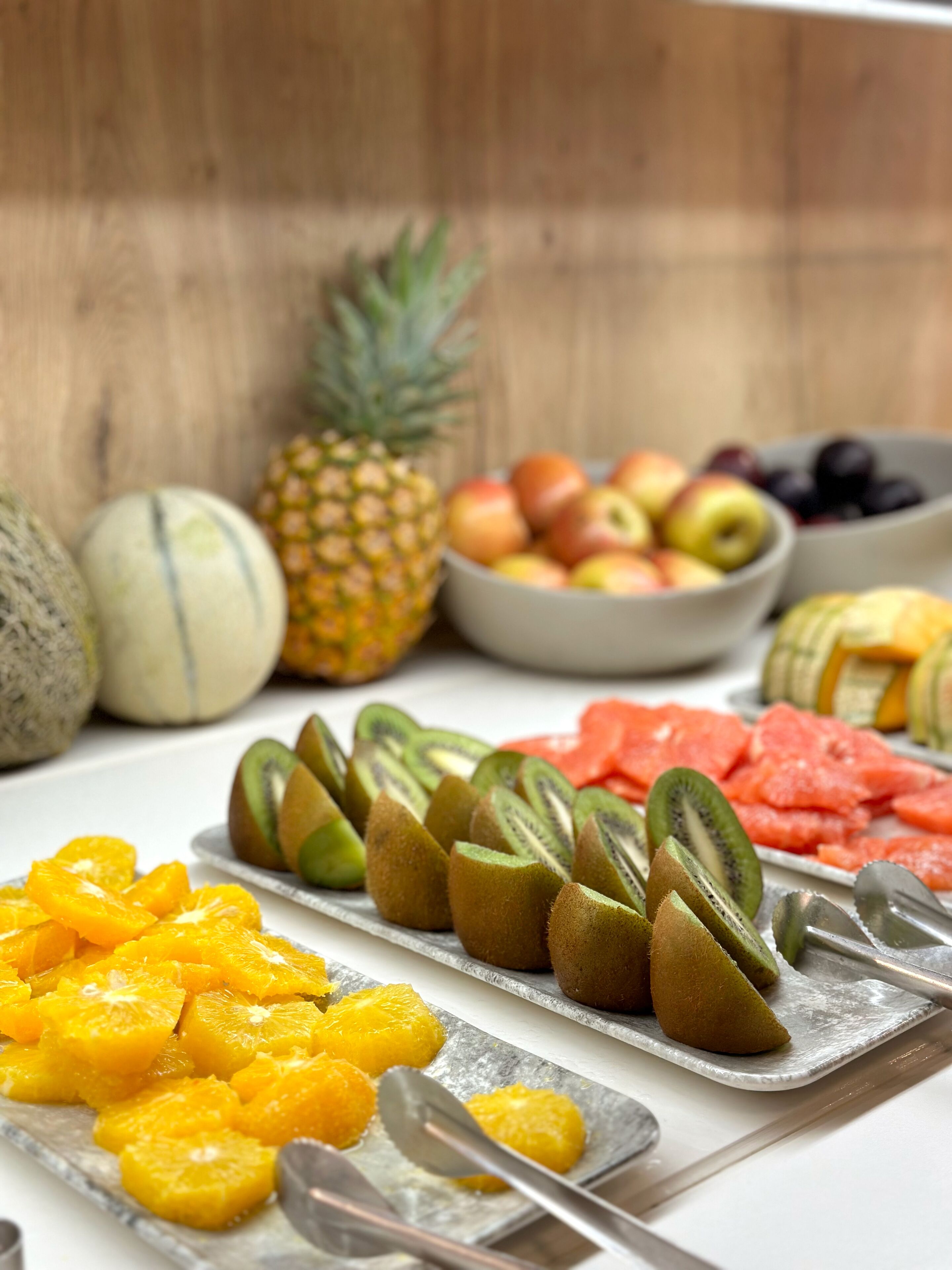 Una variedad de frutas como piña, melón, manzanas y kiwis dispuestas en una bandeja.