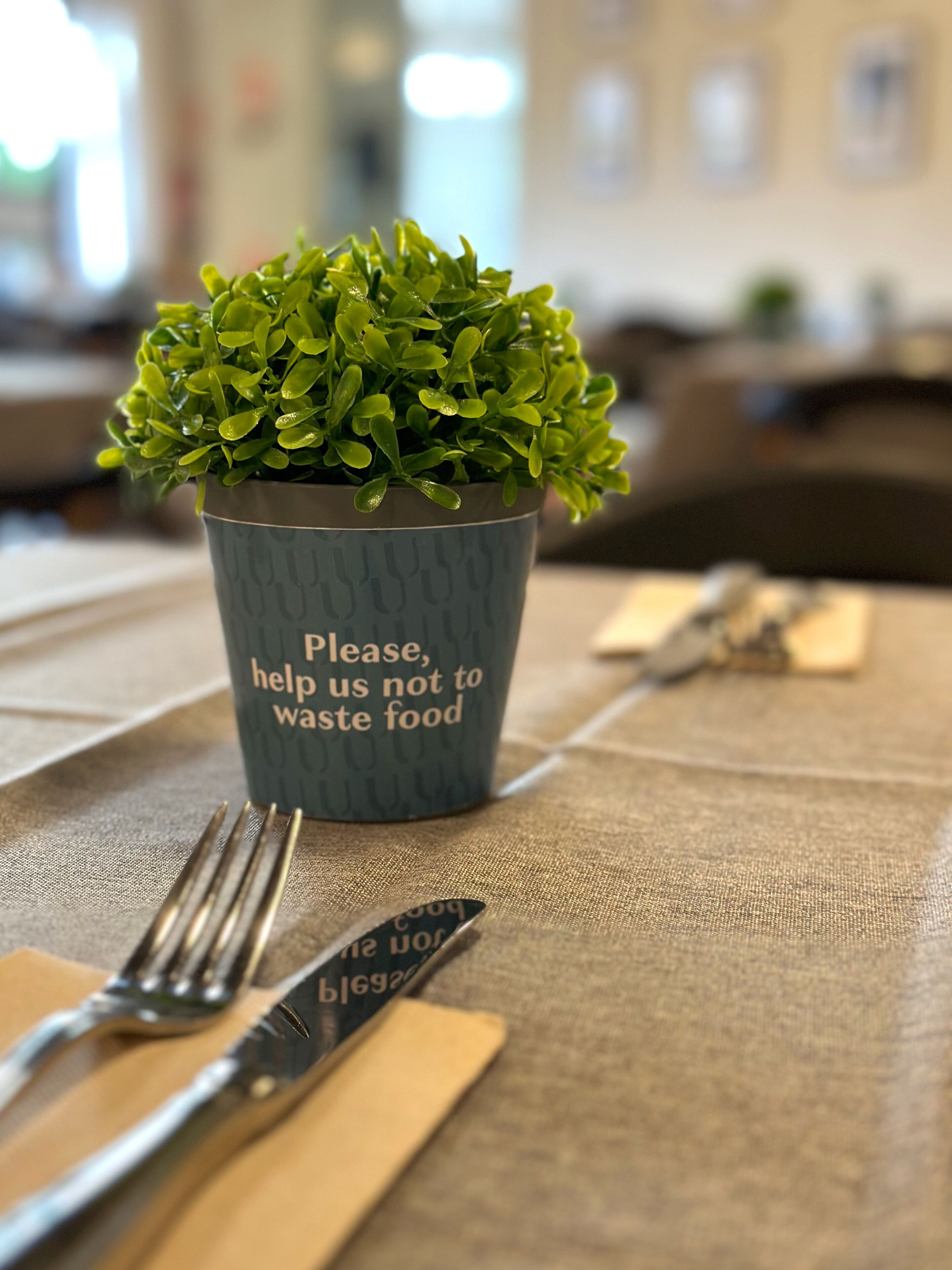 A table setting with a plant in a cup that has a message about not wasting food.