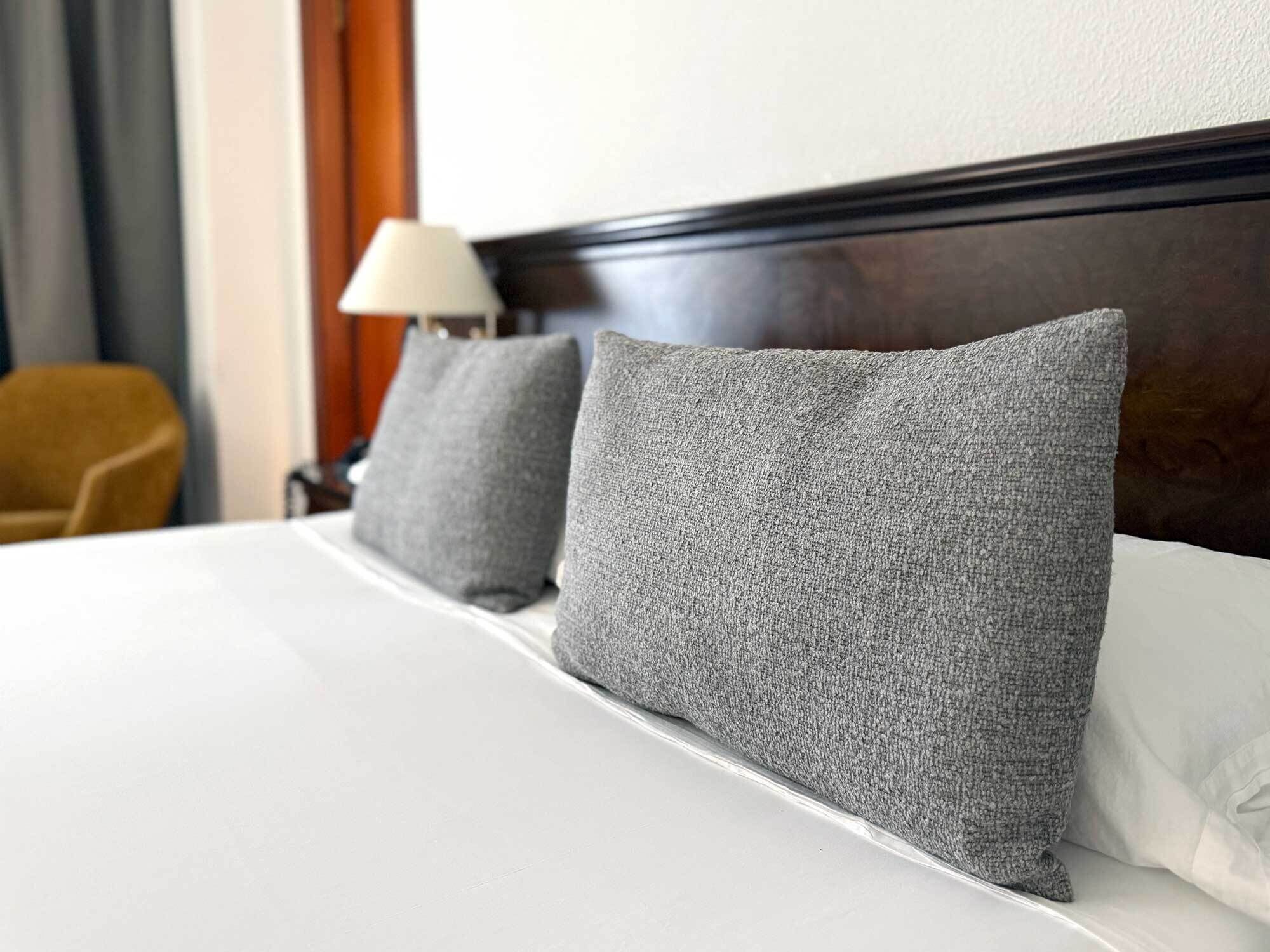 A neatly made bed with white linens and two grey pillows.