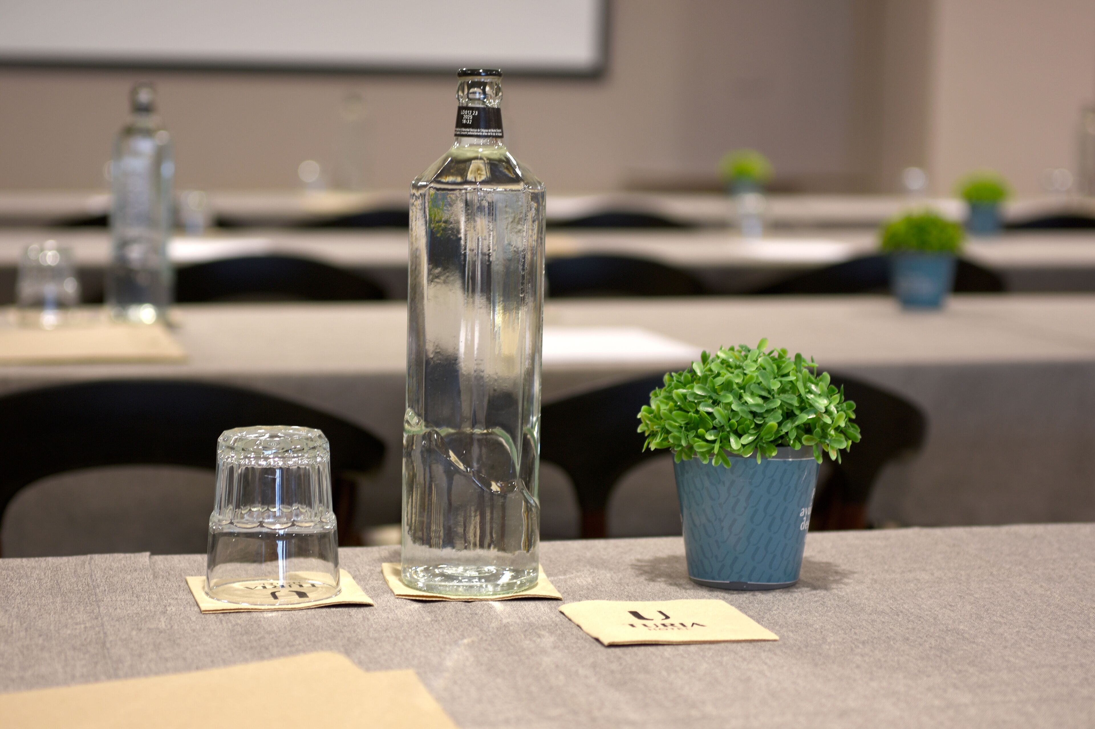Una mesa de conferencias con una botella transparente, un vaso pequeño y una planta en maceta.