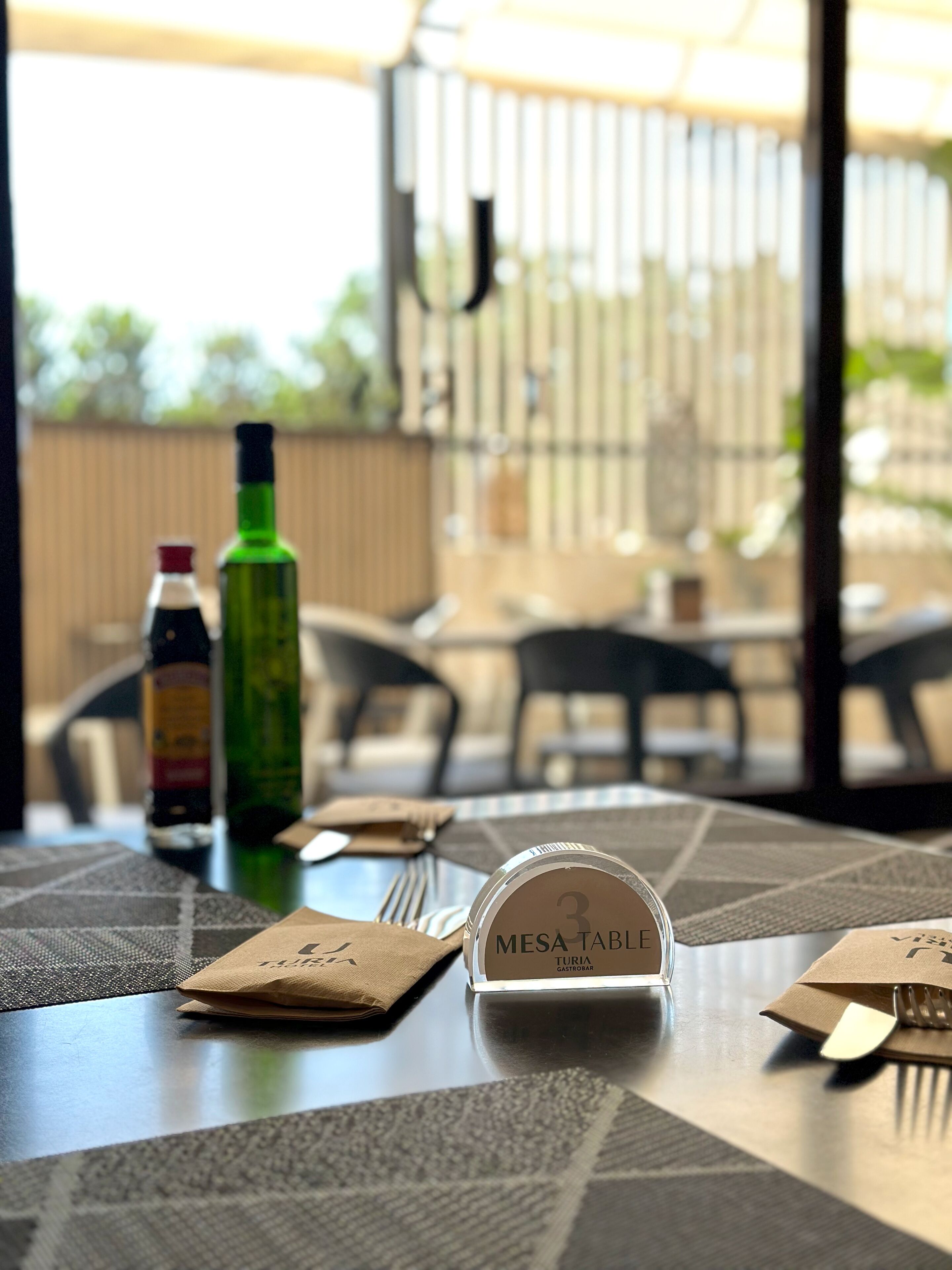 Une table à manger avec une pancarte indiquant « Mesa Table », une bouteille et une serviette sur une nappe à motifs.