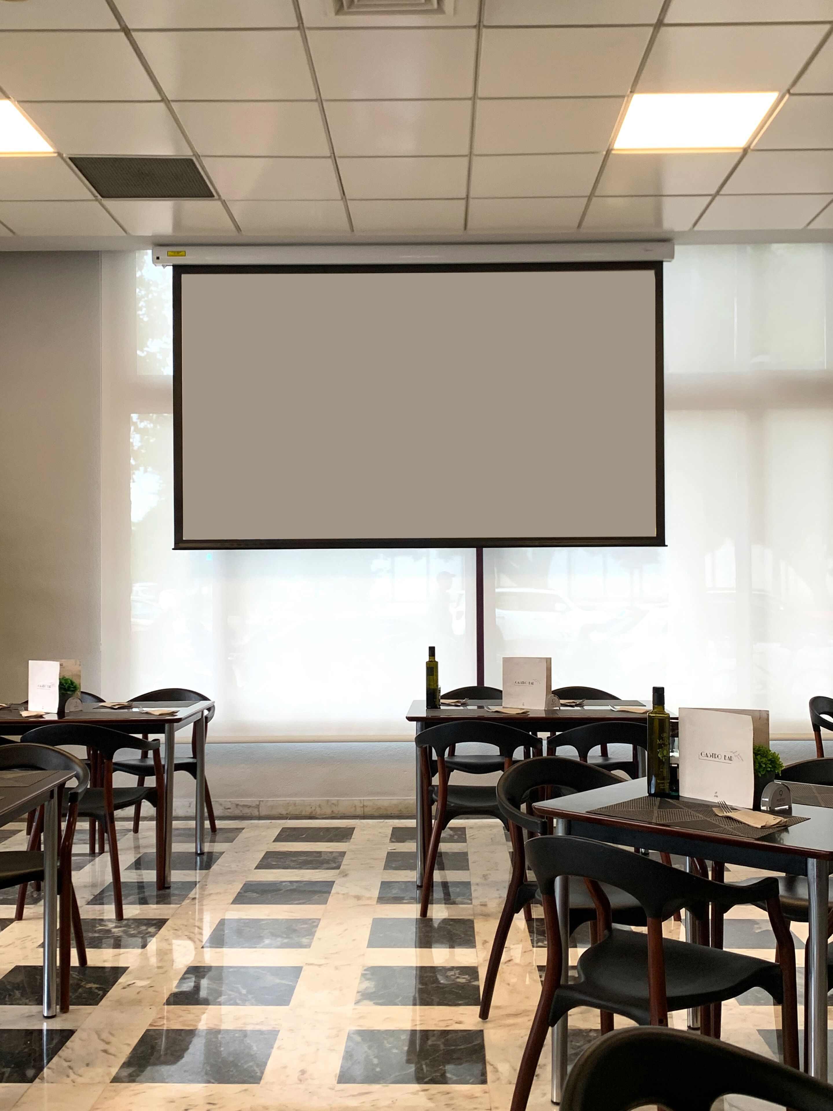 Un salón de conferencias con una amplia pantalla de proyección, mesas, sillas y un suelo a cuadros.