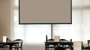Un salón de conferencias con una amplia pantalla de proyección, mesas, sillas y un suelo a cuadros.