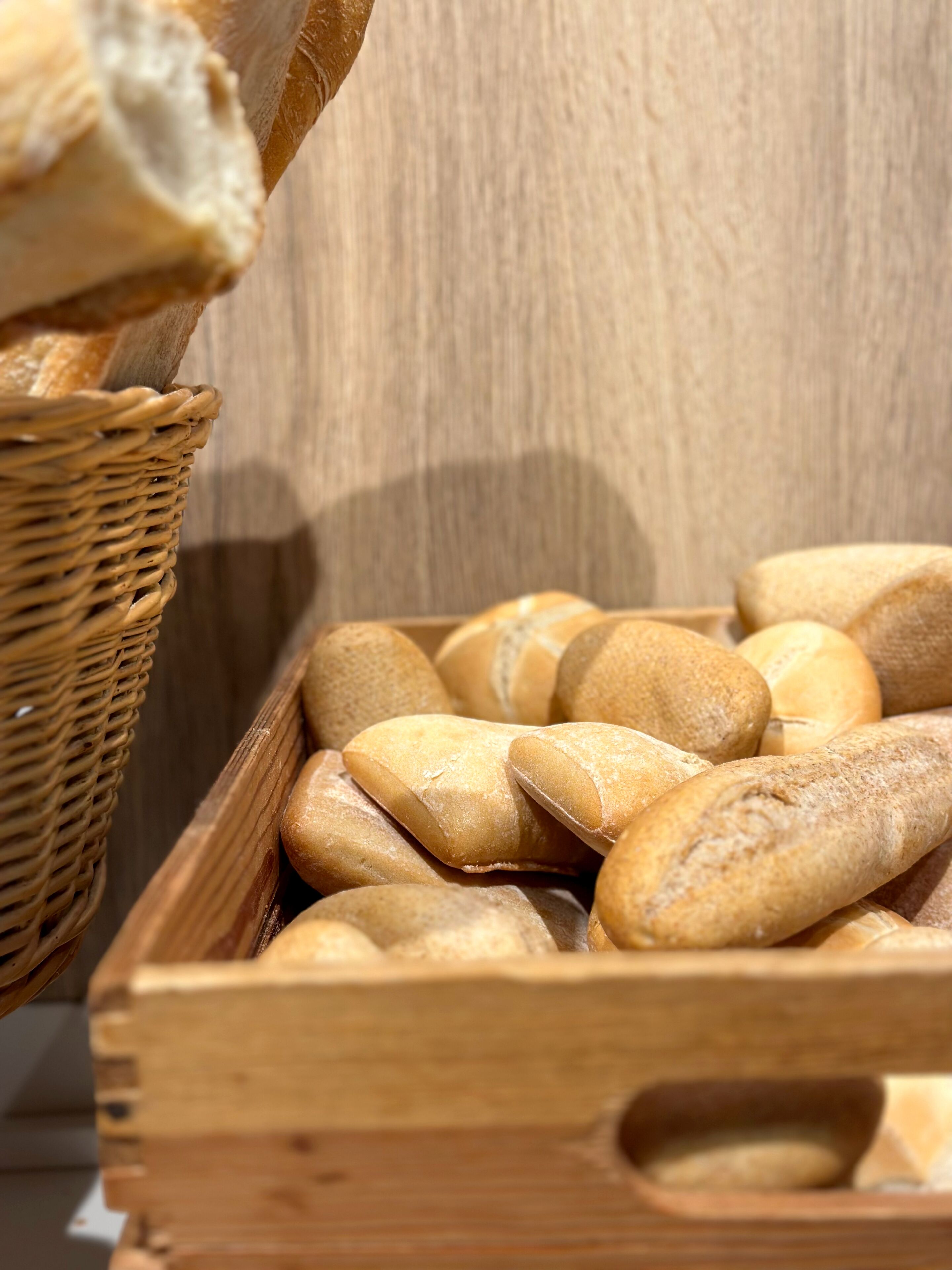 A wooden crate filled with various types of bread, including baguettes and rolls, placed on a wooden surface.