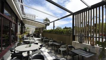 Un patio al aire libre con mesas y sillas redondas, piso a cuadros y vista a la calle.
